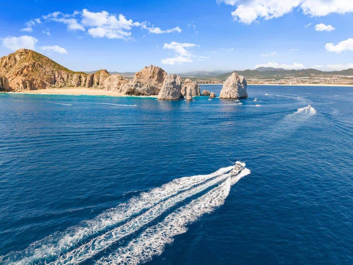 Un bateau qui laisse une vague derrière lui dans une eau d’un bleu limpide, avec des formations rocheuses et une côte visible au loin.