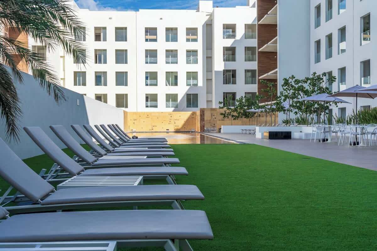 Ein moderner Hotelinnenhof mit Pool, Liegestühlen und Außenmöbeln.