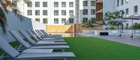Ein moderner Hotelinnenhof mit Pool, Liegestühlen und Außenmöbeln.