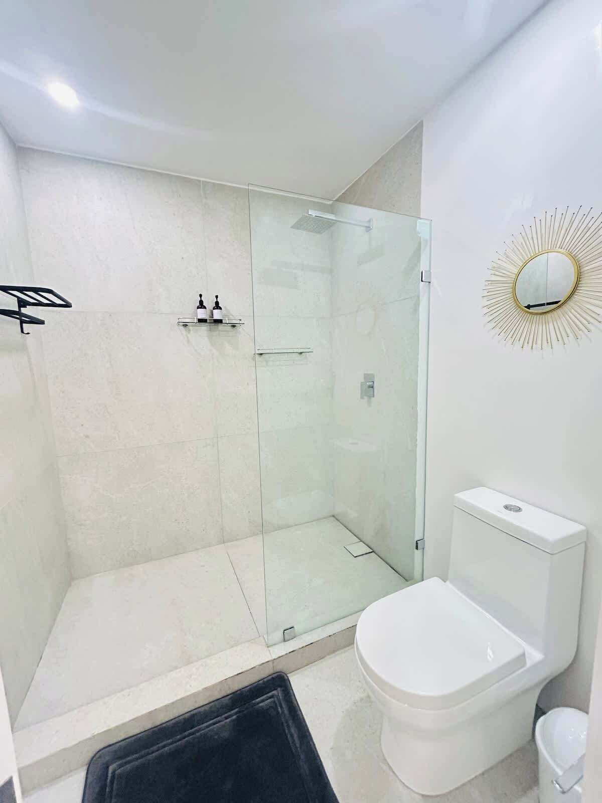 A modern bathroom with a glass shower enclosure, a white toilet, and a mirror with a sunburst design.