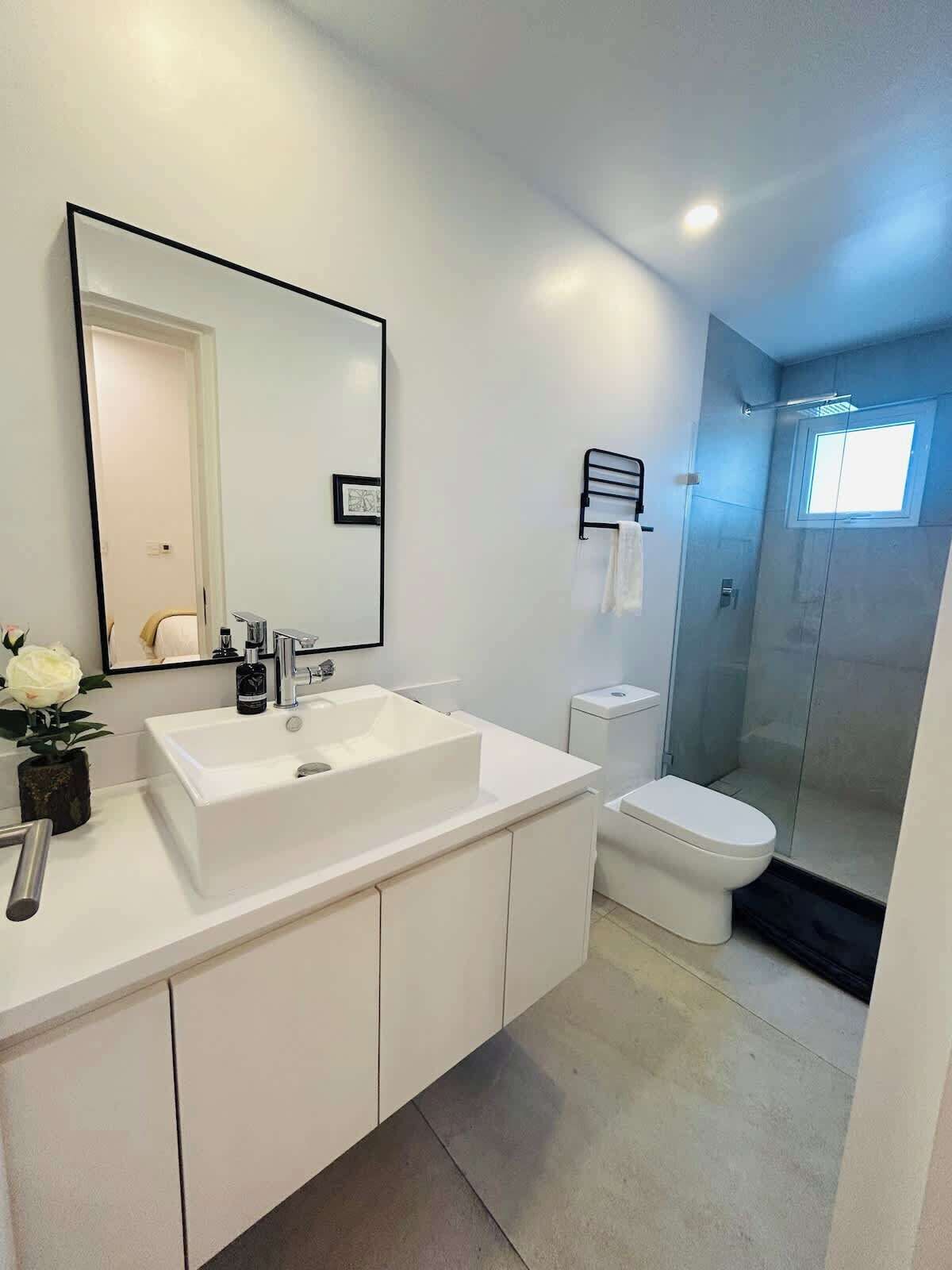A modern bathroom with a large mirror, white sink, and toilet.