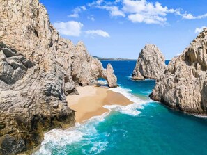 A coastal landscape with rocky cliffs, a sandy beach, and turquoise waters. - Best Location in Cabo 3BR Condo Walk to Everything (Cabo San Lucas)