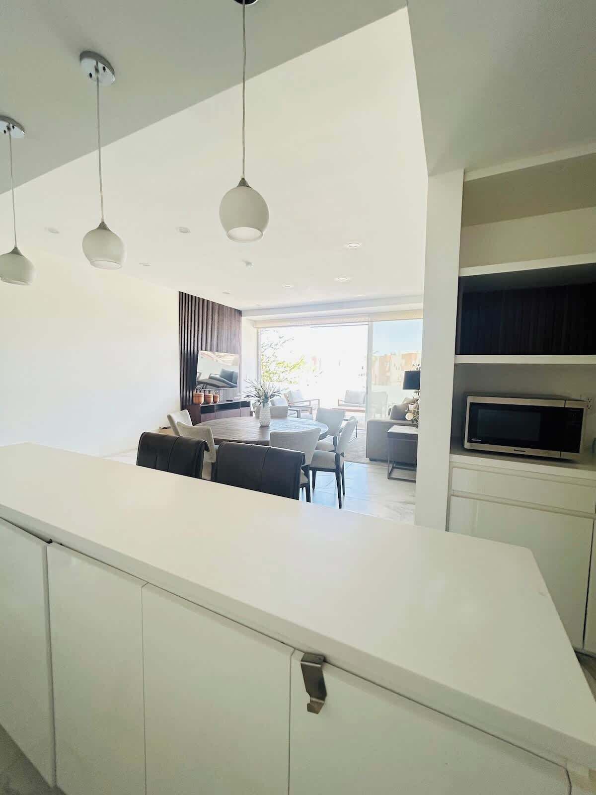 A modern kitchen with white cabinetry, a dining area with a round table and chairs, and a TV on a shelf.