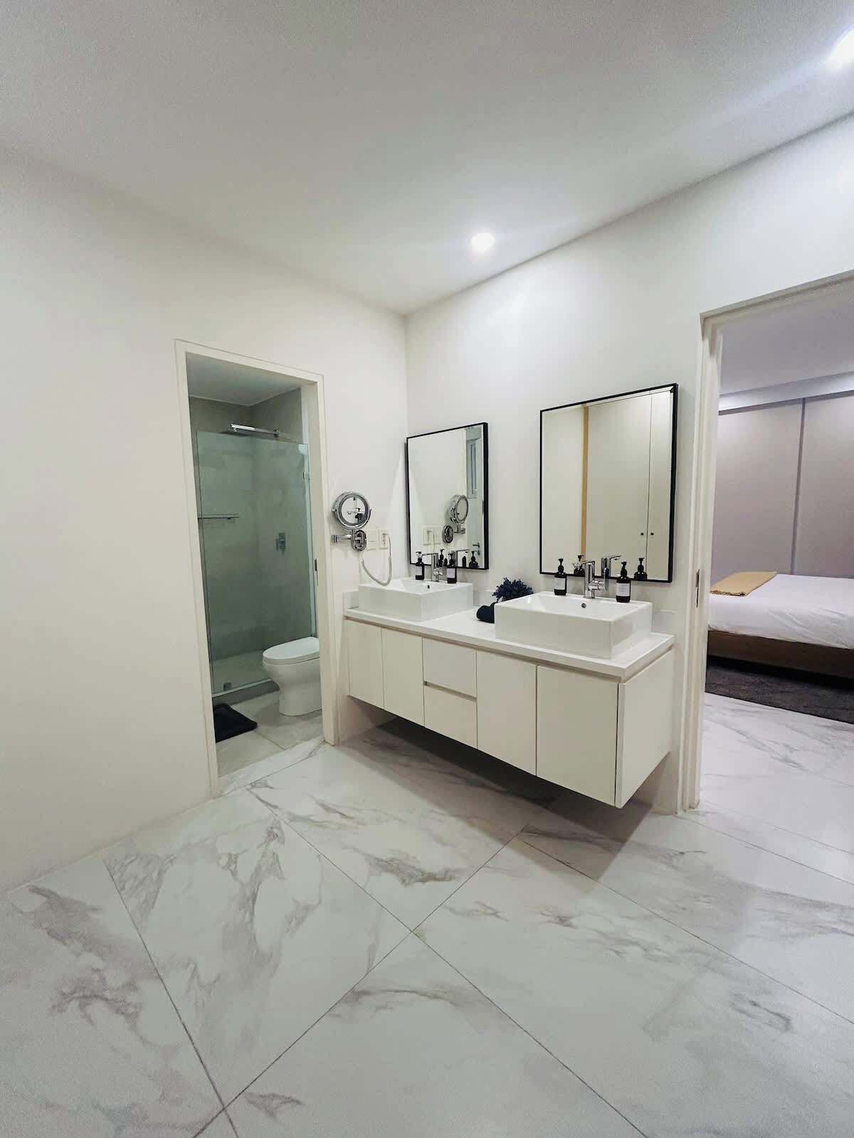 A modern bathroom with a double sink vanity, a shower, and a toilet.