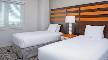 A hotel room with two beds, a window with blinds, a nightstand with a lamp, and a patterned carpet.