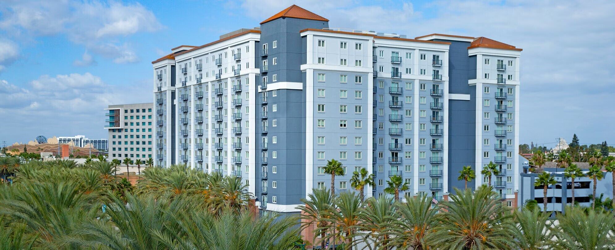 Un hotel de varios pisos con balcones, un diseño arquitectónico moderno y palmeras al frente.
