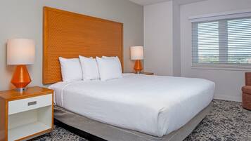 A hotel room with a large bed, two bedside tables with lamps, a window with blinds, and a patterned carpet.