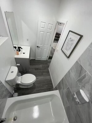 Ein Badezimmer mit Badewanne, Toilette, Waschbecken und einer Tür zu einem anderen Raum.