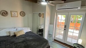 Une chambre avec un lit, un ventilateur de plafond, un appareil de climatisation et une porte-fenêtre coulissante donnant sur un espace extérieur.