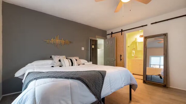 Een moderne slaapkamer met een bed, een plafondventilator, een wandlamp en een schuifdeur naar een badkamer.
