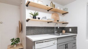 Een moderne keuken met een wit aanrecht, een RVS-gootsteen, grijze kastjes en houten planken erboven.