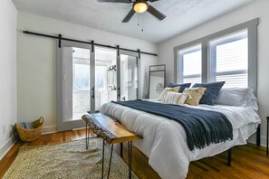 Een slaapkamer met een bed, plafondventilator, raam en deur.