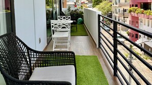 Een balkon met een zwarte rieten stoel, witte stoelen en een kleine tafel.