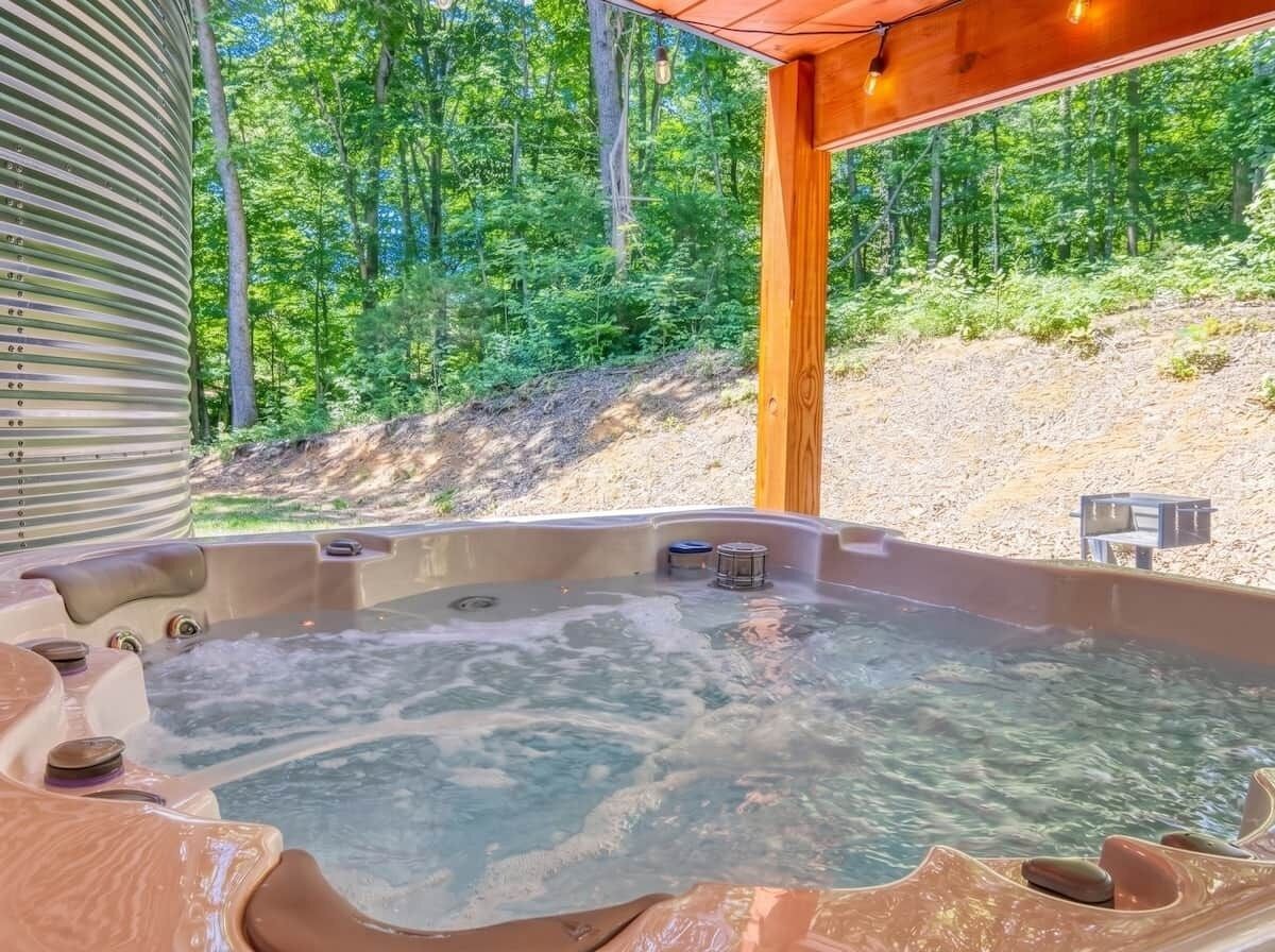 A hot tub with a wooden deck and a view of a forested hillside.
