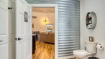 Een badkamer met een wit toilet, een prullenbak en een wandplank met toiletartikelen.