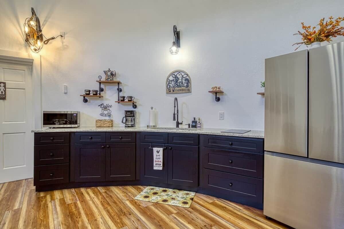 Una cucina con mobili scuri, un frigorifero in acciaio inossidabile e un pavimento in legno.