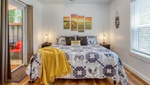 A bedroom with a bed, a ceiling fan, a window with blinds, and a door to a balcony.