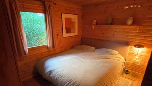 A wooden cabin bedroom with a bed, a nightstand, a window, and a ceiling light fixture.