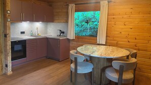 A wooden interior with a kitchen, dining area, and a window with a view of greenery.