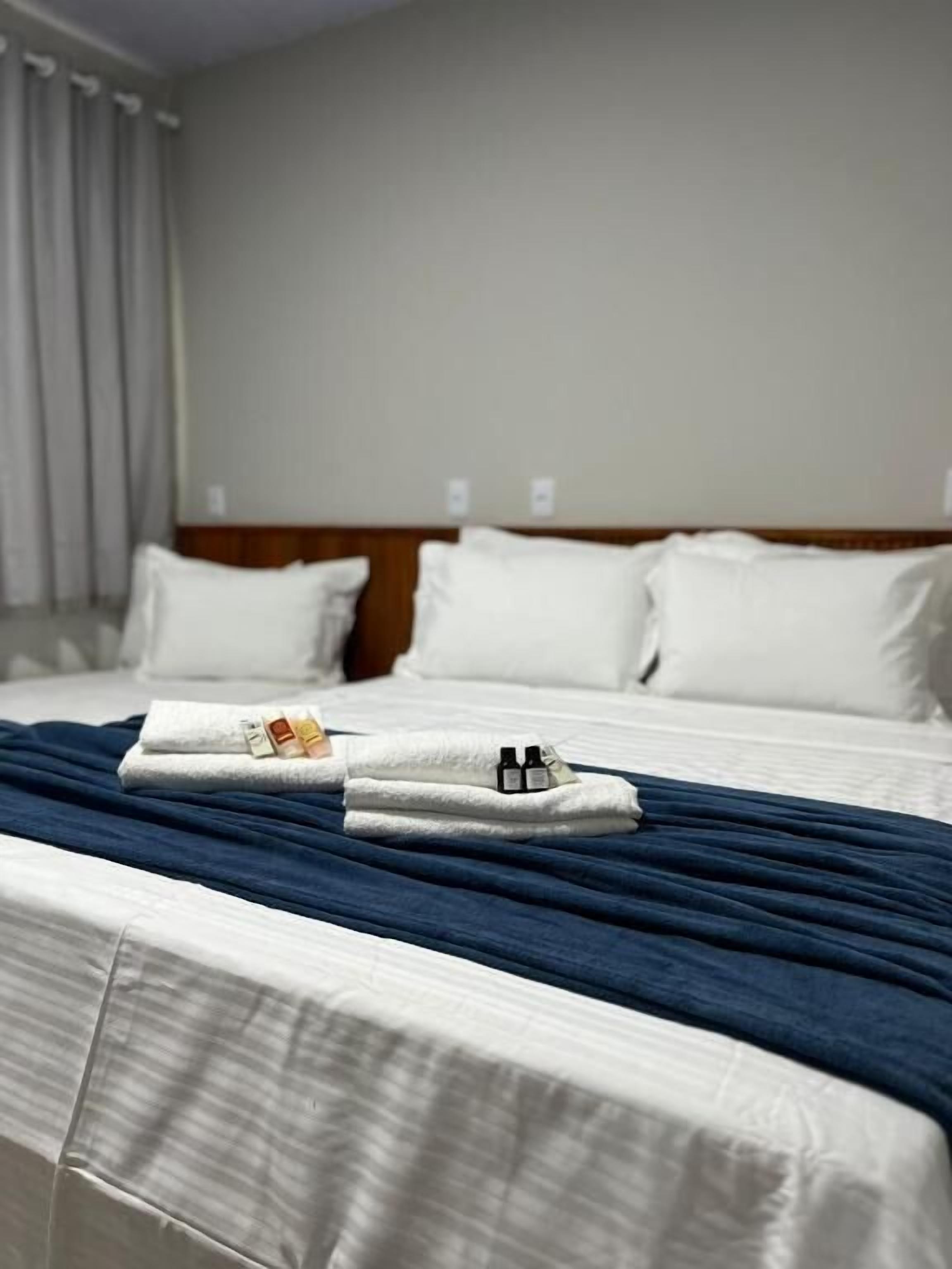 Una habitación de hotel con una cama bien hecha, cabecera de madera y una ventana con cortinas.