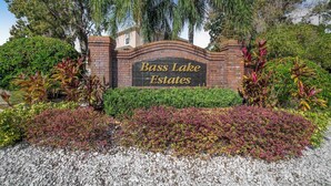 Ein Schild für Bass Lake Estates mit einem Ziegelbogen, umgeben von gepflegten Gärten und Bäumen.