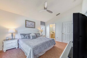 A bedroom with a bed, nightstand, lamp, ceiling fan, and a door leading to a bathroom. - Beautiful Family Villa, Heated Pool & Spa, Near Disney Parks (Kissimmee)