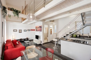 A modern living space with a red sofa, glass coffee table, and a dining area with a kitchen counter. - Vacation Home 'The Pepper in Pizzofalcone' with Balcony, Wi-Fi & Air Conditioning (Naples)