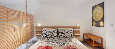 Une chambre moderne avec un lit, une tête de lit en bois et une affiche accrochée au mur.