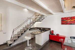 Eine moderne Küche mit integrierter Kochinsel, einem roten Schrank und einer Treppe mit Glastrennwand.