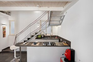 A modern kitchen with a central island, a staircase, and a red coffee machine. - Vacation Home 'The Pepper in Pizzofalcone' with Balcony, Wi-Fi & Air Conditioning (Naples)