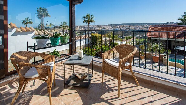A balcony with wicker furniture, potted plants, and a view of a cityscape. - CH Villa Aström La Marquesa Golf (Ciudad Quesada)