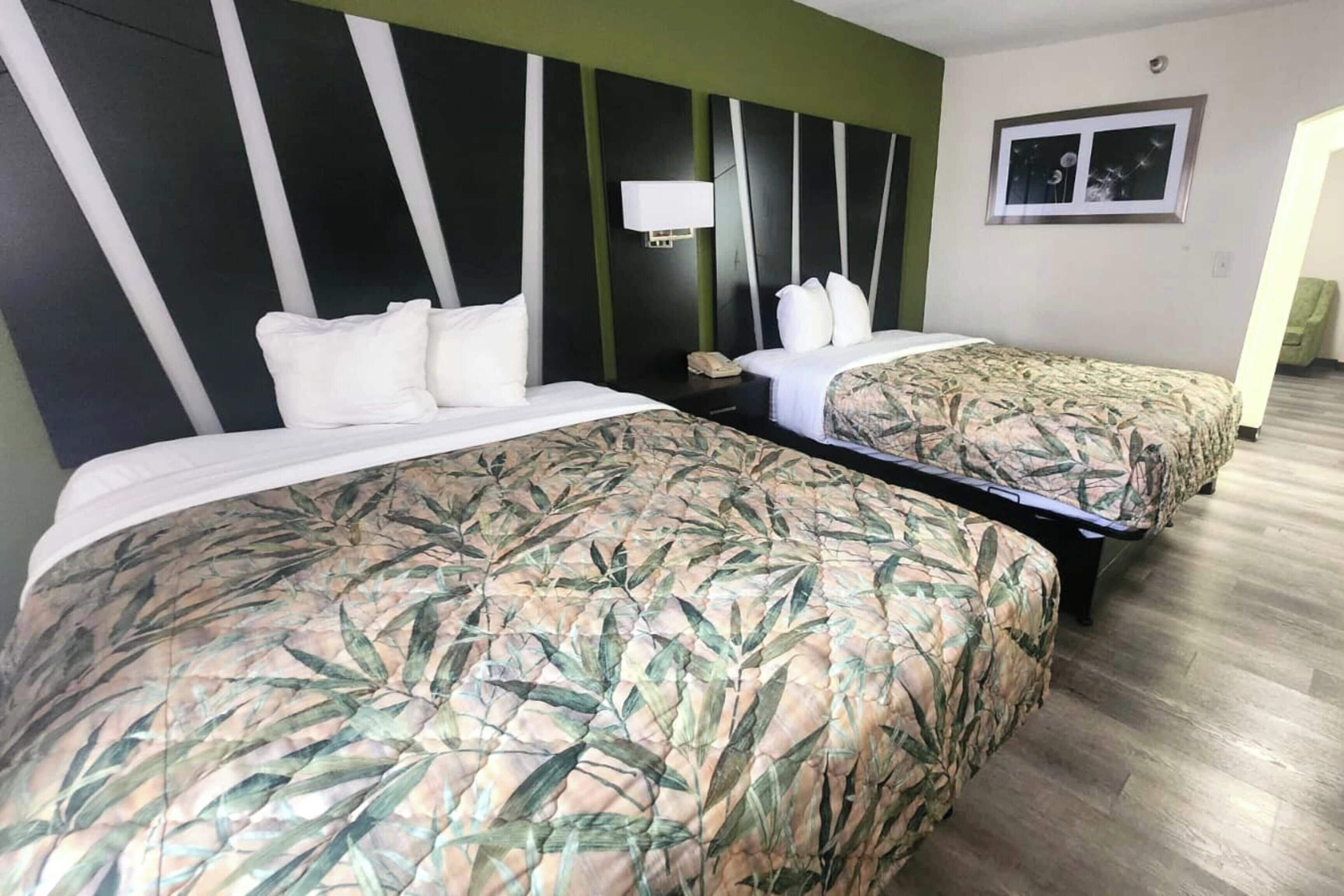 A hotel room with two beds, each with a patterned bedspread, a bedside table with a lamp, and a framed picture on the wall.