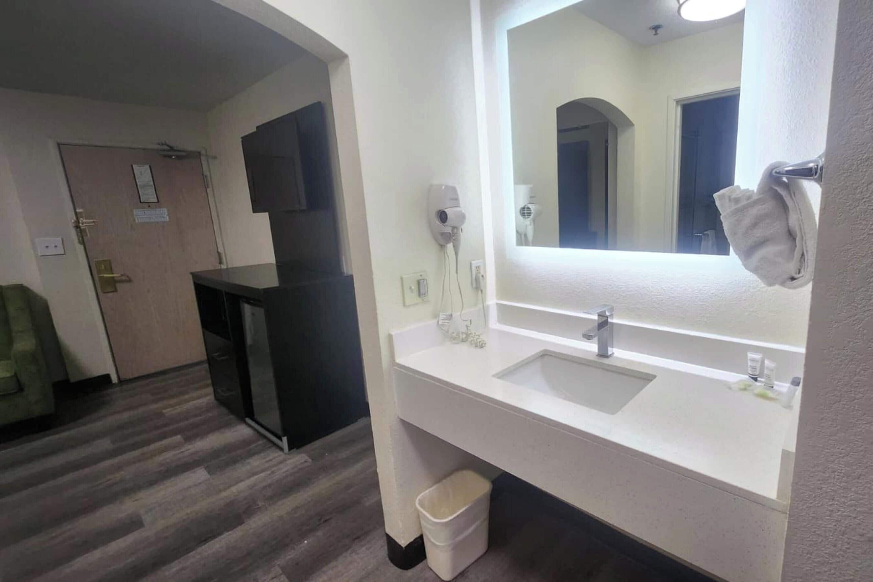 Un baño de hotel con un espejo grande, dos lavamanos, un secador de pelo y un cesto de basura.