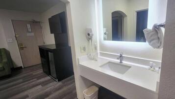 Un baño de hotel con un espejo grande, dos lavamanos, un secador de pelo y un cesto de basura.