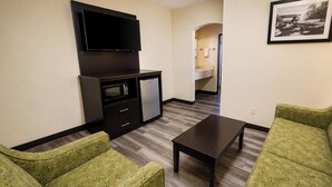A living room with a flat-screen TV, a small kitchenette, a dining table, and two patterned sofas. - Sunport Suites near Albuquerque Airport I 25 (Albuquerque)