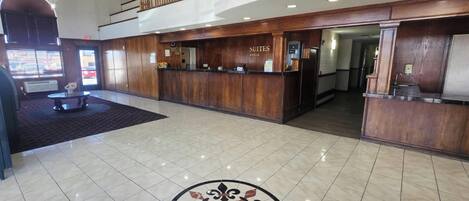 A hotel lobby with a reception desk, a staircase, and a decorative floor pattern.