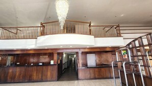 Ein Hotel-Empfangsbereich mit einer prächtigen Kronleuchter, einem hölzernen Empfangstresen und einer Treppe, die in einen oberen Bereich führt.