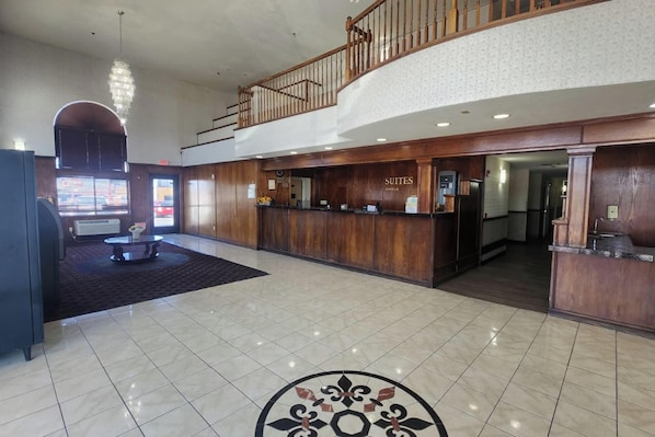 A hotel lobby with a reception desk, a staircase, and a large chandelier.