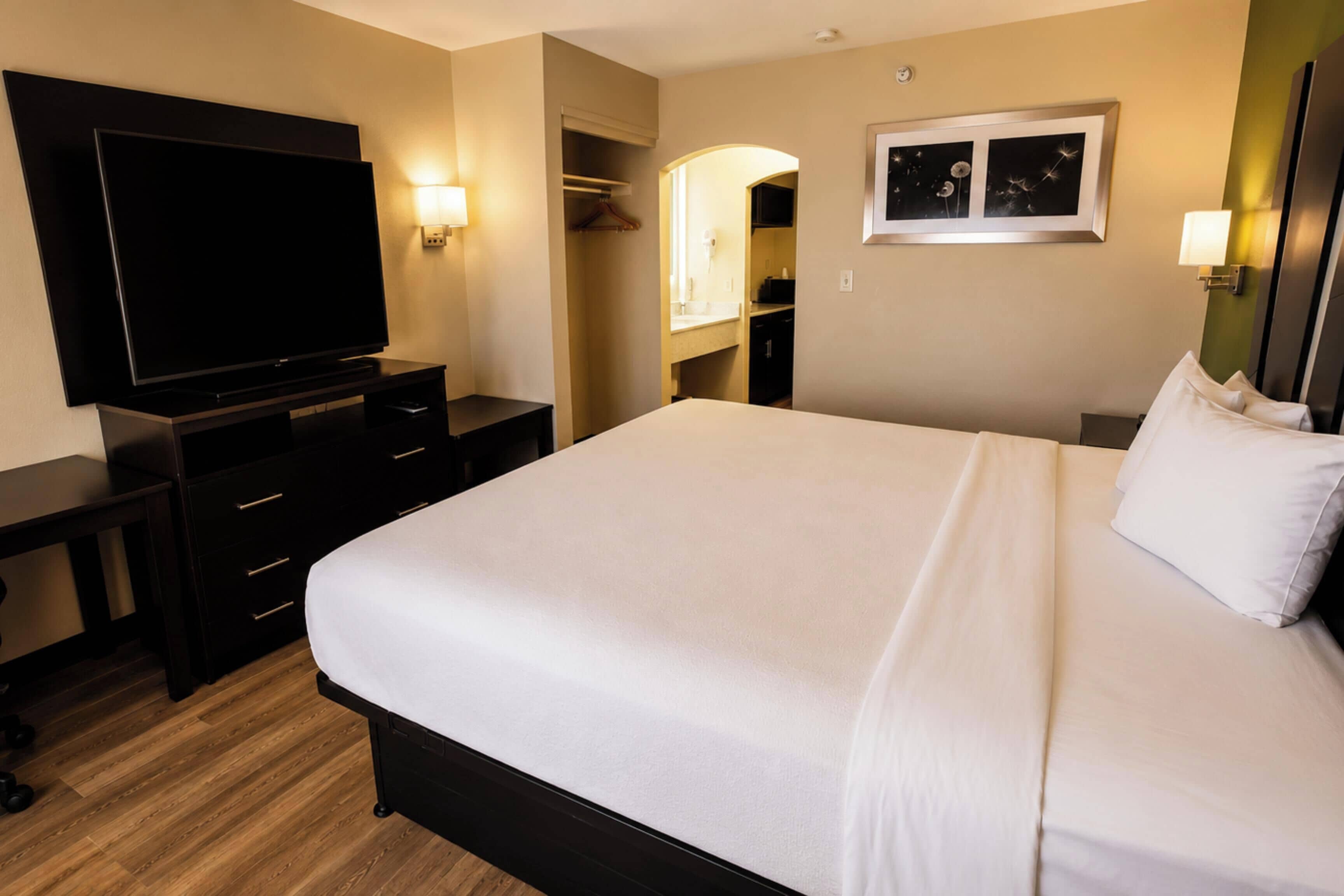 Una habitación de hotel con una cama grande, una televisión de pantalla plana, un armario y un espejo.