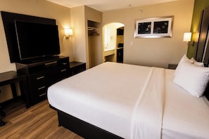 A hotel room with a large bed, a flat-screen TV, a wardrobe, and a mirror. - Sunport Suites near Albuquerque Airport I 25 (Albuquerque)