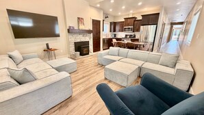 A modern living room with a flat-screen TV, grey sofas, a fireplace, and a kitchen with dark cabinets and stainless steel appliances. - Dawson Cottage Dog friendly, close to town (McCall)