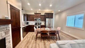 A modern kitchen with dark wood cabinets, stainless steel appliances, and a dining area with a table and chairs. - Dawson Cottage Dog friendly, close to town (McCall)