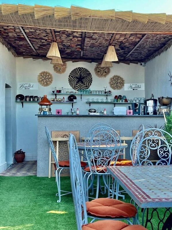 An outdoor patio with a metal table and chairs, a thatched roof, and decorative wall art. - Riad Omi Winna (Marrakech)