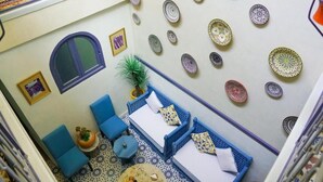 A room with a blue sofa set, a small table, a potted plant, and a wall decorated with various plates. - Riad Omi Winna (Marrakech)