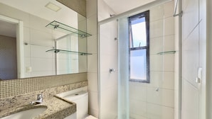 Un baño con cabina de ducha de vidrio, inodoro, lavabo con encimera de granito y un espejo grande.