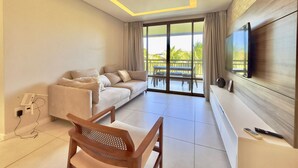 Una sala de estar moderna con un sofá, una silla de madera, un televisor de pantalla plana y un balcón con mobiliario exterior.
