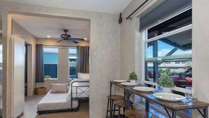 Una camera compatta con un letto, un tavolo da pranzo con sedie, una ventola a soffitto e una finestra con vista sull'esterno.