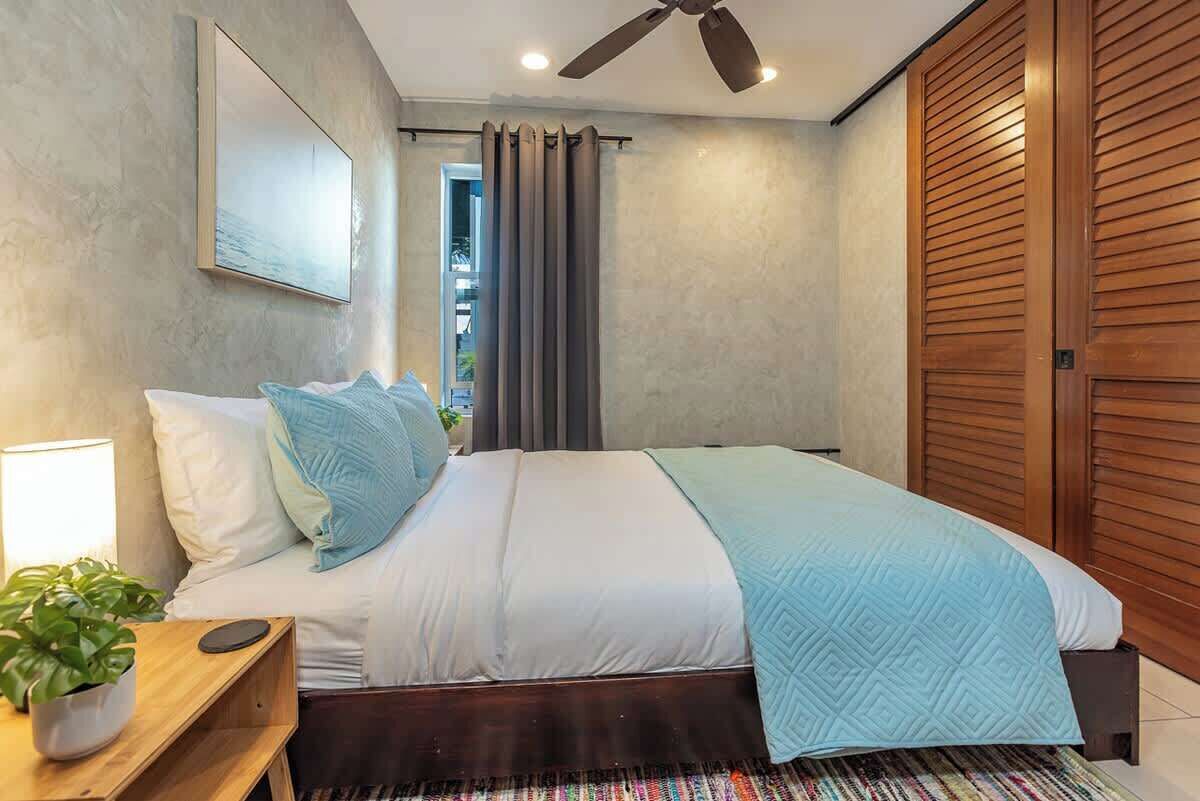 Une chambre à coucher avec un lit, un ventilateur de plafond, une table de chevet avec une lampe et une fenêtre avec des rideaux.