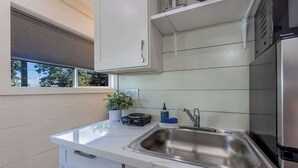 Une cuisine moderne dot ée d’un évier en acier inoxydable, d’une fenêtre avec stores, d’une plante en pot et d’un réfrigérateur compact.