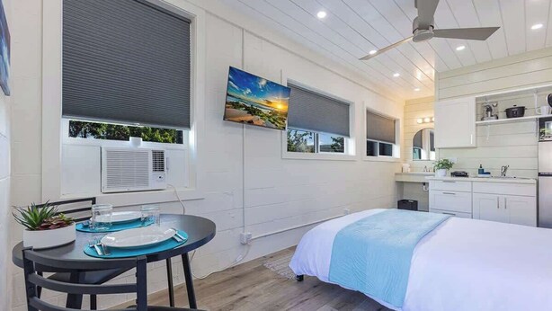 Une chambre moderne comprenant un lit, une table à manger avec des chaises, un ventilateur de plafond et un coin cuisine.